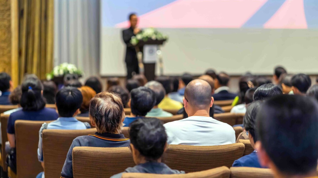 Back side of audience listening the Speaker with podium on the stage in the conference hall